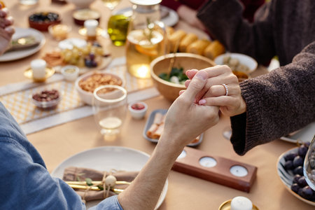 Caucasian middle aged woman and man holding hands across table during meal, hands clasped in gesture of affection, surrounded by food and drinksの写真素材