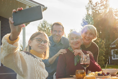 Caucasian girl taking selfie with middle aged Caucasian man, senior Caucasian woman, and middle aged...