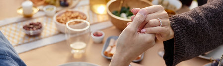 Header of middle aged woman holding hands with middle aged man at dining table, hands intertwined in...