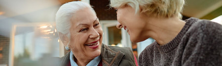 Header of Senior Caucasian woman smiling and talking with middle aged Caucasian woman outdoors, both women facing each other and sharing joyful moment, close up on faces, candid interactionの写真素材