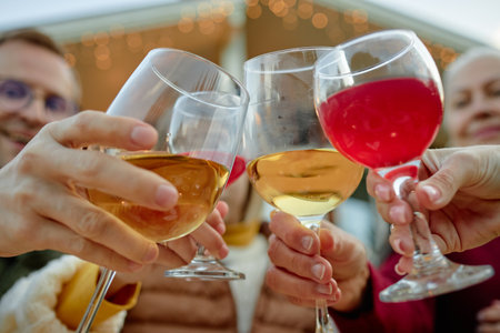 Group of diverse people clinking glasses outdoors, celebrating together, hands and faces partially...