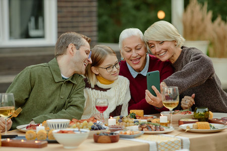 Caucasian middle aged man, child, senior woman, middle aged woman sitting at outdoor table smiling...