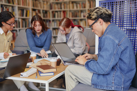 Group of multiethnic teenagers collaborating on project, working with laptops and notebooks in library setting, focused on studying and sharing ideas around tableの写真素材