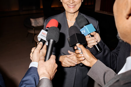 Middle aged Caucasian woman smiling while standing in front of multiple microphones held by...