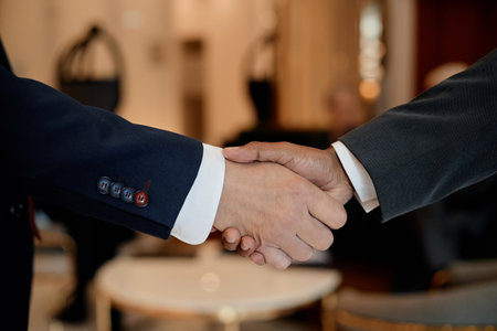 Caucasian man and Black man shaking hands in business setting, only hands and part of arms visible,...