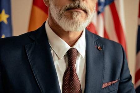 Middle aged man wearing suit and tie standing in front of international flags, showing partial face and upper body, displaying formal appearance and professional demeanorの写真素材