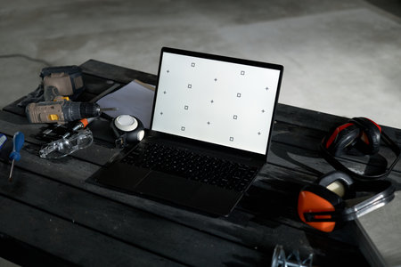 Laptop with blank calibration screen standing on wooden table surrounded by power drill,...