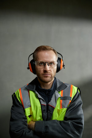 Portrait of middle aged Caucasian man wearing safety glasses and earmuffs standing with arms crossed...