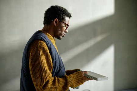 Middle aged Black man standing in profile holding color swatches, wearing glasses, on construction siteの写真素材