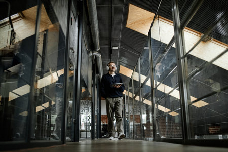 Middle aged Caucasian man walking through modern business office corridor holding digital tablet,...