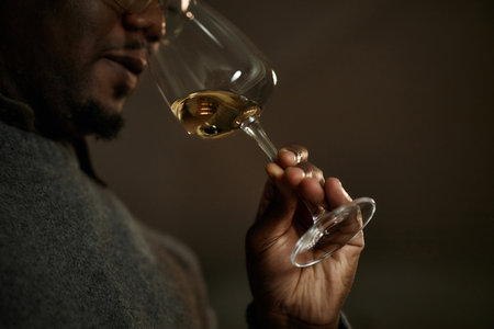 Black middle aged man holding wine glass, smelling aroma of wine during tasting session, focusing on sensory evaluation, close up of hand and face in profileの写真素材