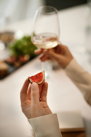 Caucasian young adult woman holding glass of wine in one hand and fresh fig slice in other hand during wine tasting session, focusing on sensory evaluation and food pairingの写真素材