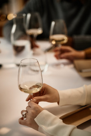 Caucasian young adult woman holding wine glass, participating in wine tasting with multiethnic group of adults, hands visible on table, engaging in sensory evaluation of wineの写真素材