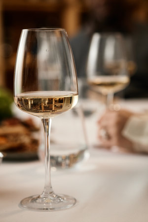 Hand holding wine glass while tasting wine at table, another wine glass and blurred figure in background suggesting wine tasting sessionの写真素材