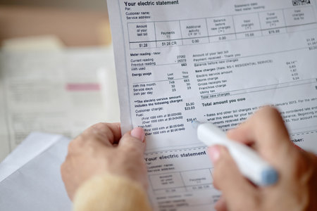 Adult woman holding pen reviewing utility bill and invoice documents at desk, focusing on analyzing charges and payment details, hands in close upの写真素材