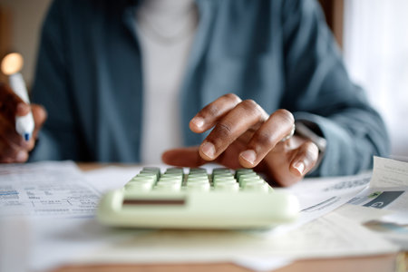Person analyzing invoices and bills using calculator, hand pressing calculator buttons while reviewing financial documents on desk, focusing on managing personal or business expensesの写真素材