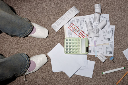 Adult woman standing near scattered invoices, bills, calculator and envelopes on carpet, analyzing overdue payments with documents marked past due on floorの写真素材