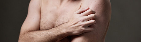 Man holding upper arm with hand, showing bare torso and chest, demonstrating concern about skin...