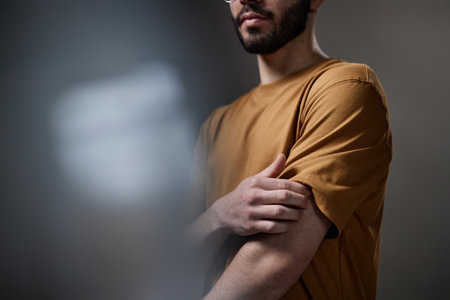 Young adult Caucasian man touching arm while waiting for dermatologist consultation, standing in clinical setting, partial face visible, neutral expression, not looking at cameraの写真素材