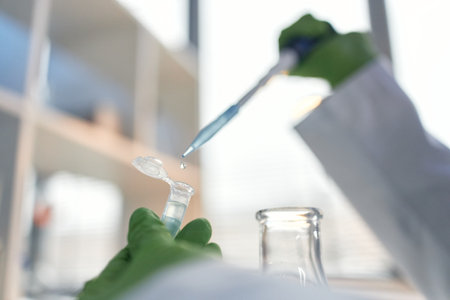 Scientist wearing green gloves transferring liquid with pipette into microcentrifuge tube in...