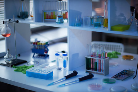 Laboratory table displaying scientific glassware, test tubes with colored liquids, pipettes, petri dishes and vials arranged for chemical or biological research experimentの写真素材
