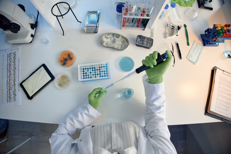Top view of person scientist working in laboratory using pipette with test tubes, petri dishes, microscope and scientific equipment on tableの写真素材
