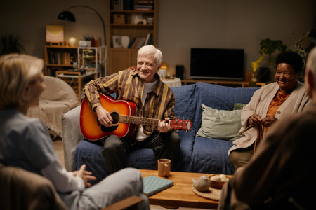 Group of seniors including man playing acoustic guitar and smiling, woman and senior woman sitting together and listeningの写真素材