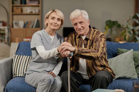 Portrait of Caucasian senior man sitting on sofa holding cane next to smiling Caucasian middle aged...