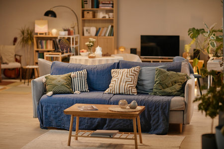 Empty living room showing cozy seating area with sofa covered by multiple patterned pillows, wooden...