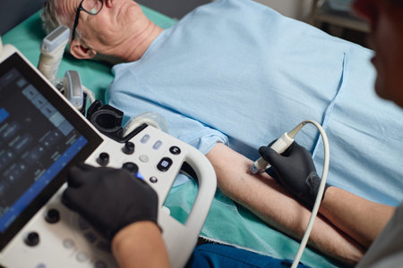 Senior Caucasian man lying on hospital bed undergoing vascular ultrasound examination by male healthcare professional using medical imaging device in vascular centerの写真素材