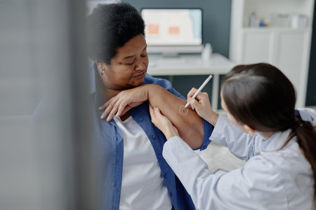 Middle aged Black woman receiving dermatological examination from young Caucasian female doctor circling lesion on arm in clinical setting, focusing on skin health assessmentの写真素材