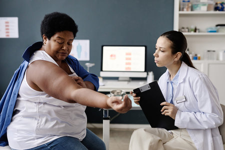 Middle aged Black woman showing arm to young adult Caucasian female doctor during dermatology consultation, doctor holding clipboard and attentively examining patient in medical officeの写真素材