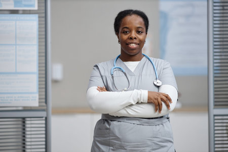 Portrait of young adult Black woman standing with arms crossed wearing medical scrubs and...