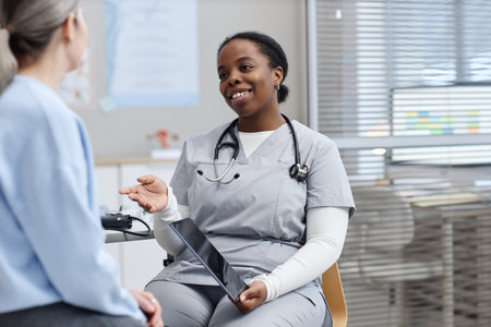 Smiling Black woman young adult doctor sitting and talking with Caucasian middle aged woman patient...