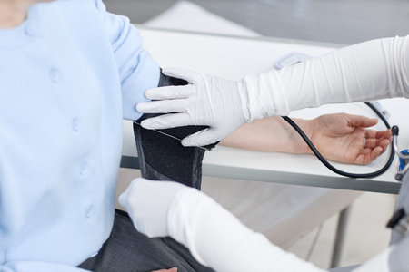 Caucasian middle aged woman receiving blood pressure measurement from medical professional wearing...