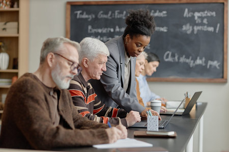 Black young adult woman assisting group of middle aged and senior Caucasian men and women working on...