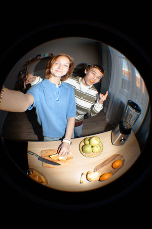 Teenage girl smiling while slicing apple on cutting board next to teenage boy making hand gesture,...
