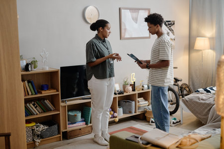 Young Black woman social worker standing and talking with teenage Black boy holding clipboard in...