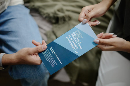 Young adult woman handing informational brochure about social care and protection to teenager during...