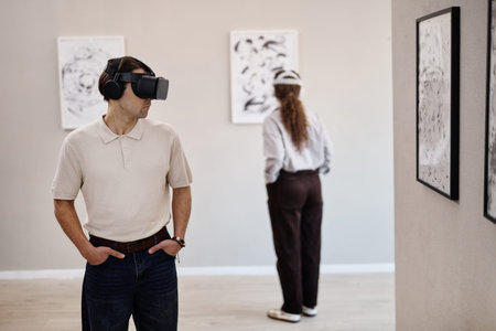 Caucasian young adult man wearing virtual reality headset standing in art gallery, looking to side...