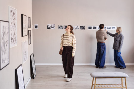 Young adult Caucasian woman walking through art gallery, middle aged Caucasian man and senior woman...