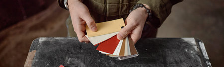 Website header shot of unseen Caucasian young adult man holding color swatches in hands, standing...