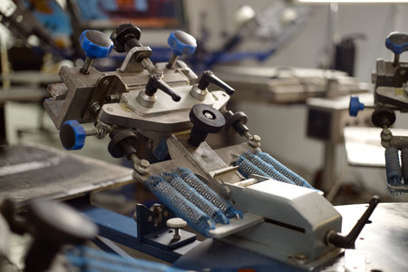 Closeup showing industrial screen printing machine with multiple adjustable clamps and levers,...