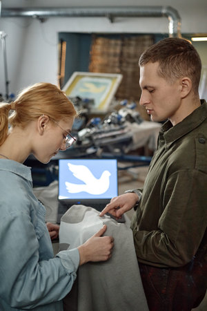 Vertical shot of Caucasian young woman and Caucasian young man examining fabric together in...