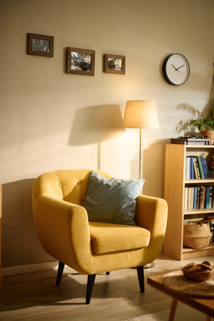 Vertical shot of empty armchair standing beside floor lamp and bookshelf in living room, suggesting home comfort and interior styling. Useful for furniture retail, home decor, real estate marketing