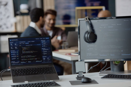 Close up of software development workstation displaying code dashboards while young adult coworkers collaborating in information technology office. Ideal for tech team, coding, cybersecurity marketing