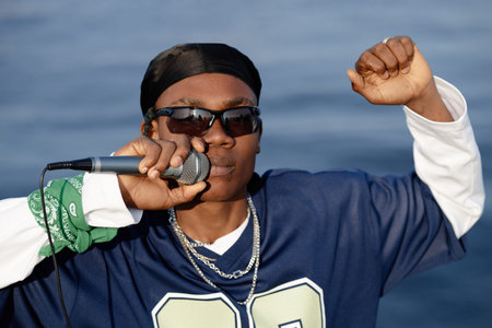 Portrait of young Black man wearing sunglasses holding microphone and raising fist while performing outdoors, confident facial expression, looking directly into camera