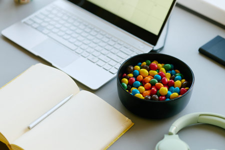 Close up of laptop, notebook, headphones, candy bowl arranged on desk, suggesting snacking during online work or study. Suitable for remote work, productivity, break time marketing