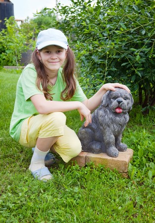 Smiling little girl near to concrete dog in gardenの写真素材