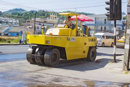 PHUKET, THAILAND - MAR 03, 2015: Workers operating asphalt paver machine and heavy machinery during...